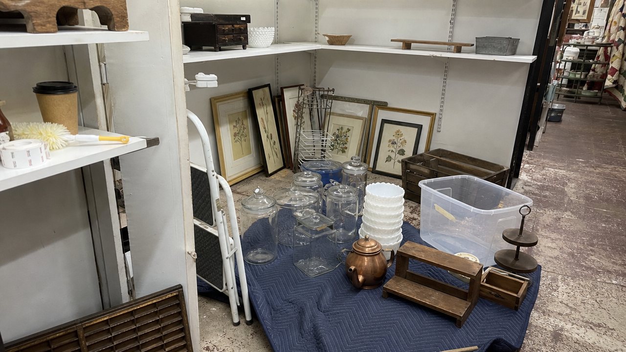 Antique mall booth in the middle of a reset with glassware and prints moved to the floor.