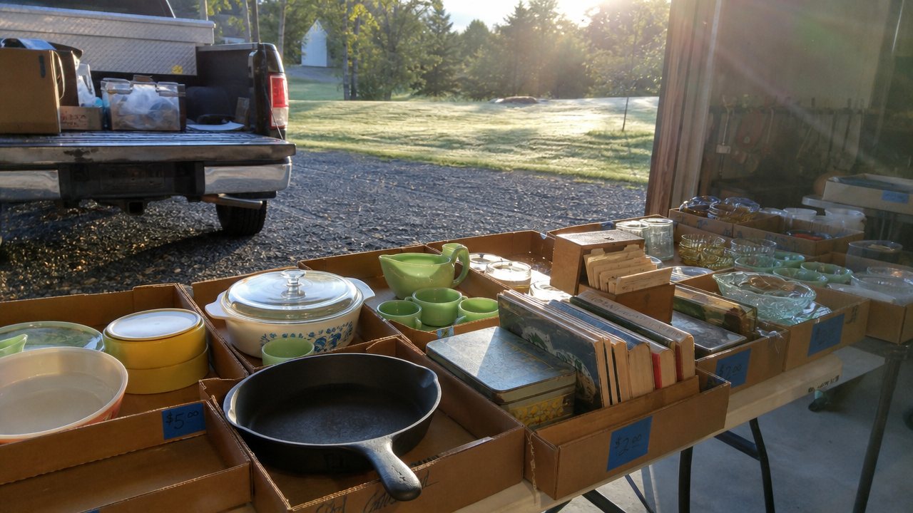 Early morning estate sale in a rural garage with tables of vintage kitchenware and cast iron.